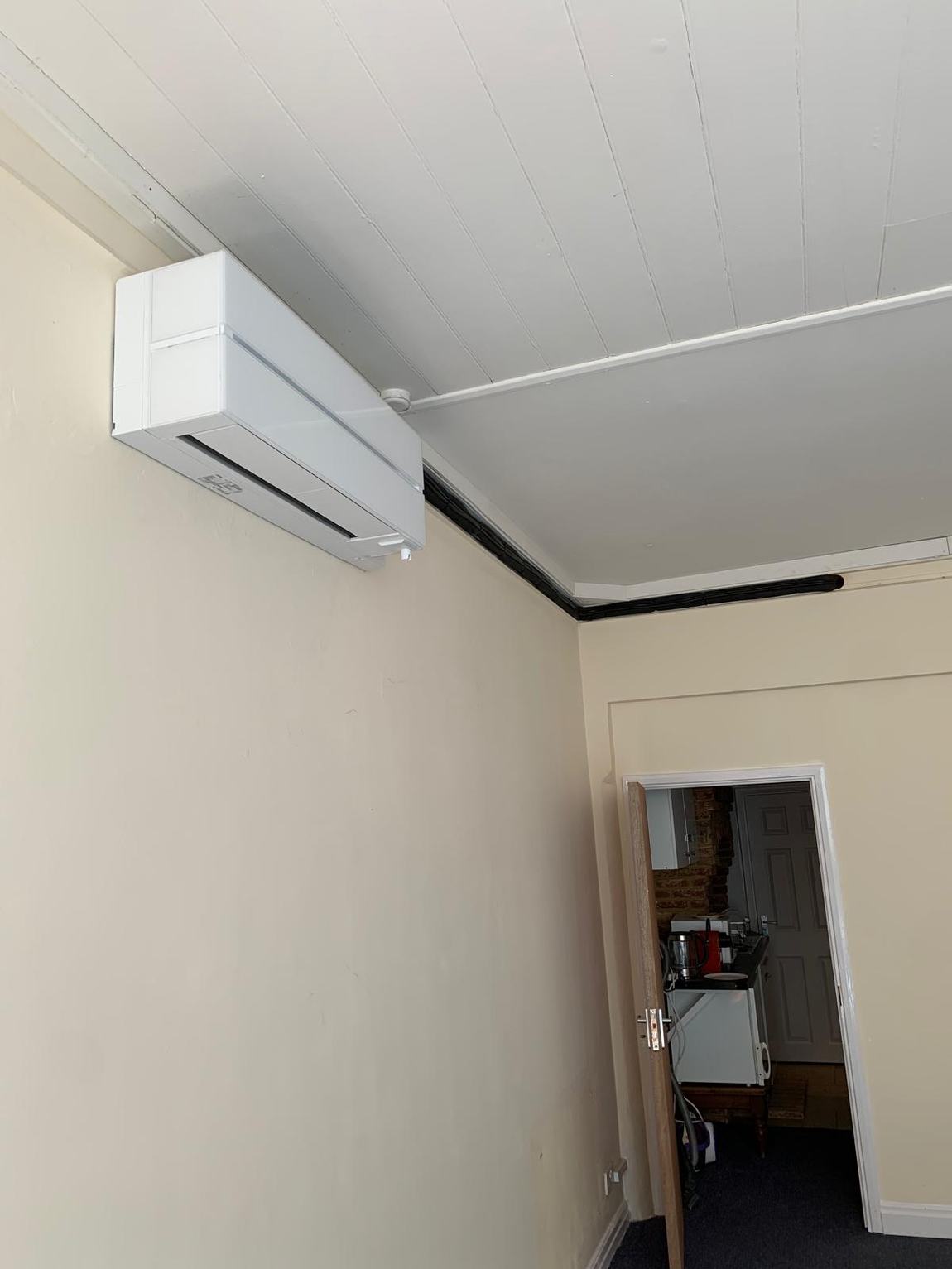 A wall-mounted air conditioning unit installed in the bare, unrenovated shop