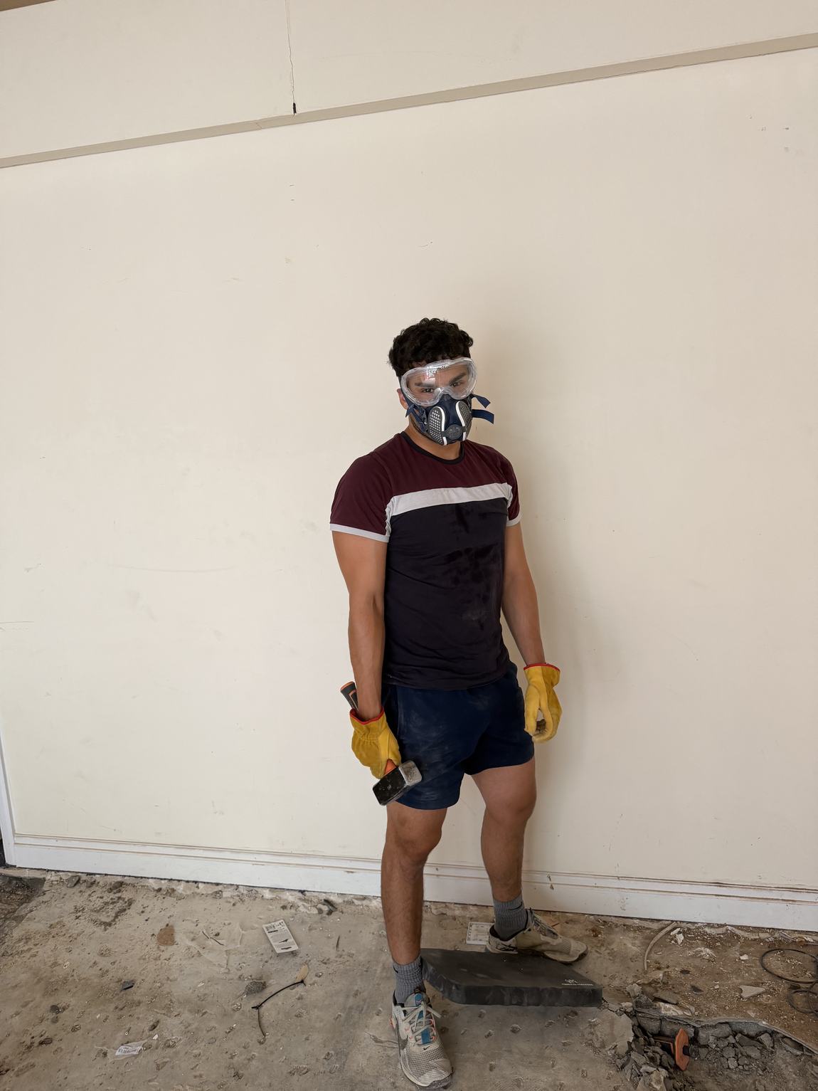 Ramin in respirator and goggles holding a sledgehammer